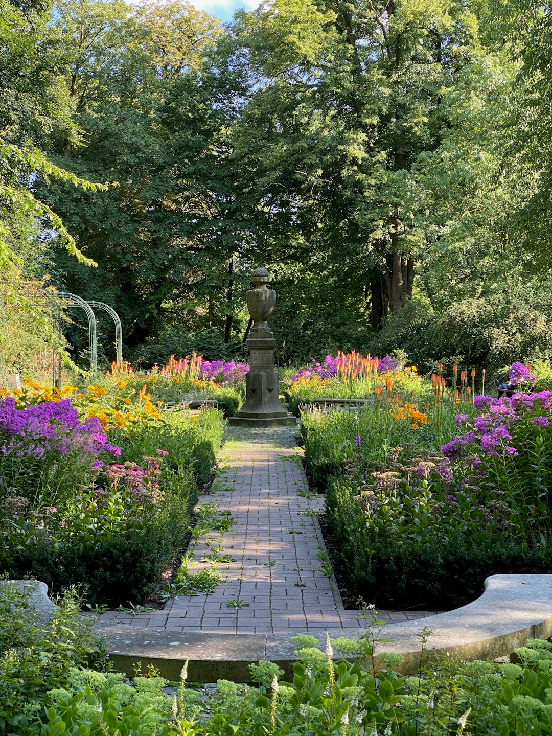 Brick path through formal garden with blooming flowers and hedges.
